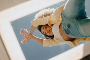 A woman with a mirror on top of her, looking down, reflecting on identity and the signs she's living someone else's life