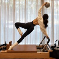 A woman doing Pilates with all of her Pilates Bag Essentials beside her